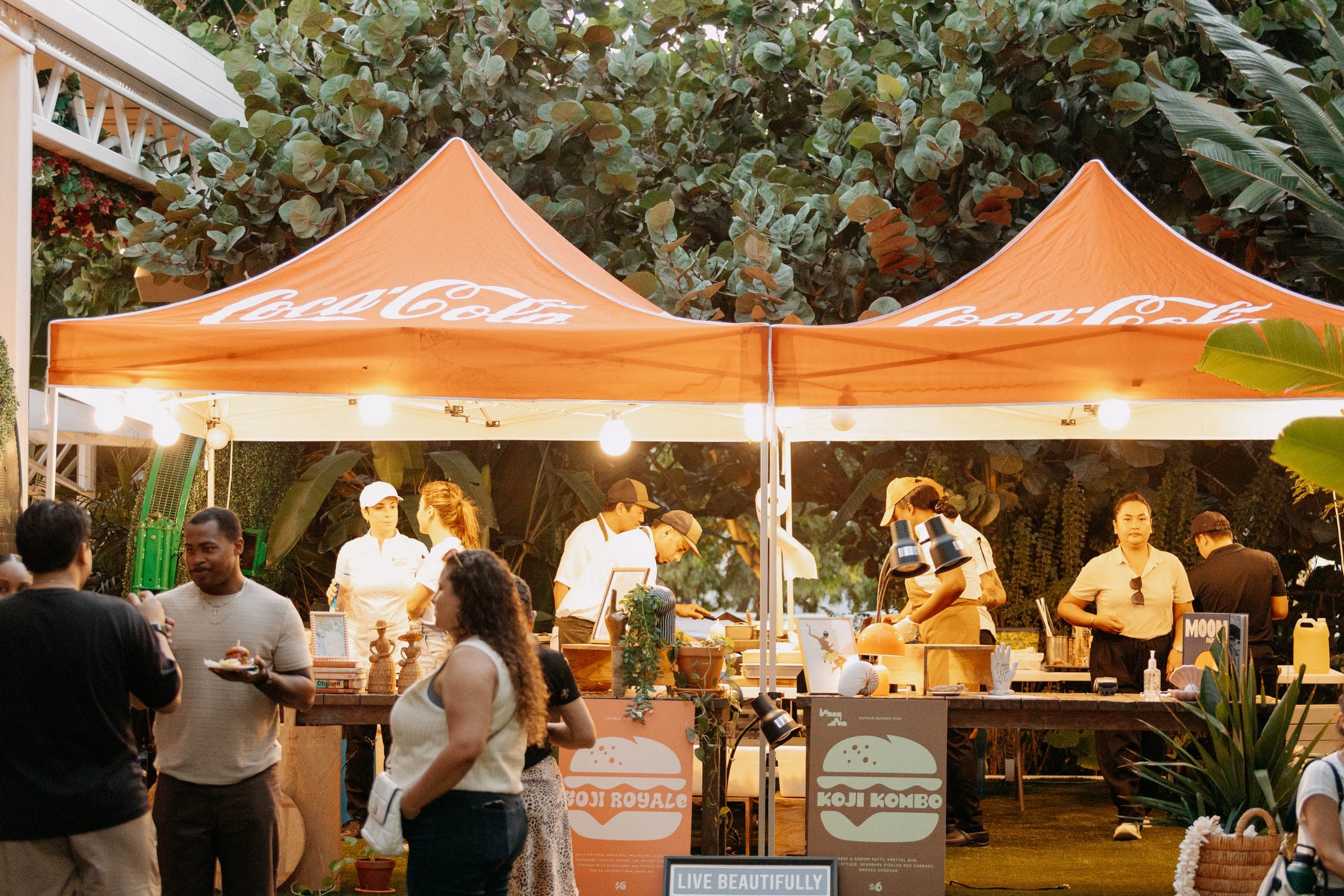 Chefs serving sliders under two Coca-Cola tents at dusk as guests line up