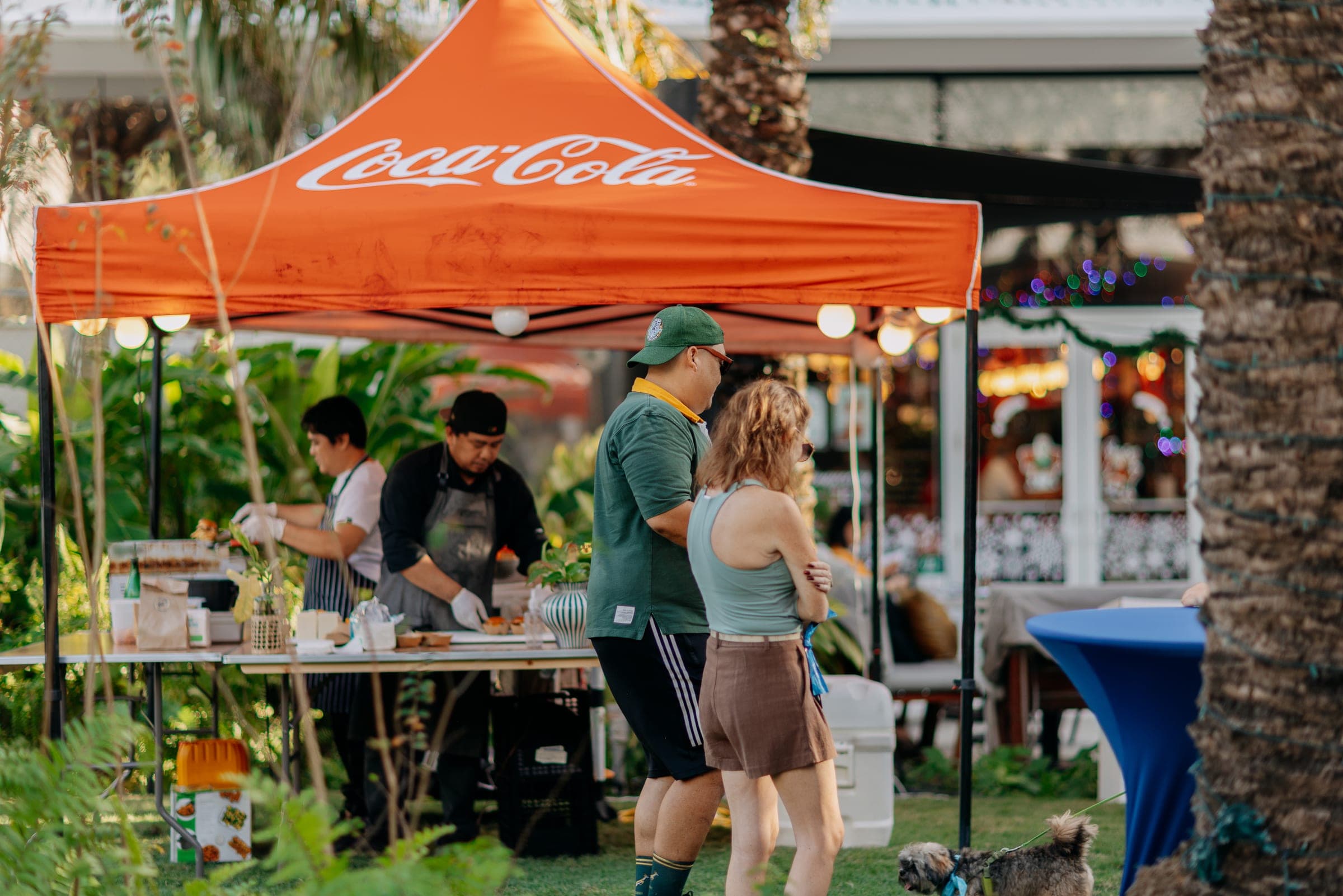 Chefs preparing food under a Coca-Cola tent as guests walk up to taste in a tropical garden