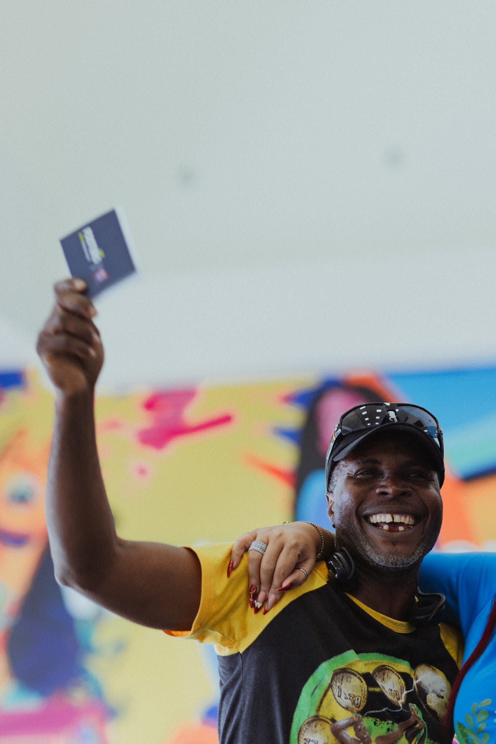 A smiling customer raising the gift card he won in front of a colourful mural