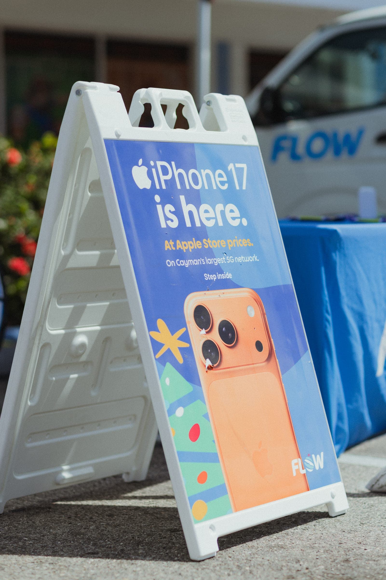 A sidewalk sign reading iPhone 17 is here, with orange iPhone artwork and Flow branding
