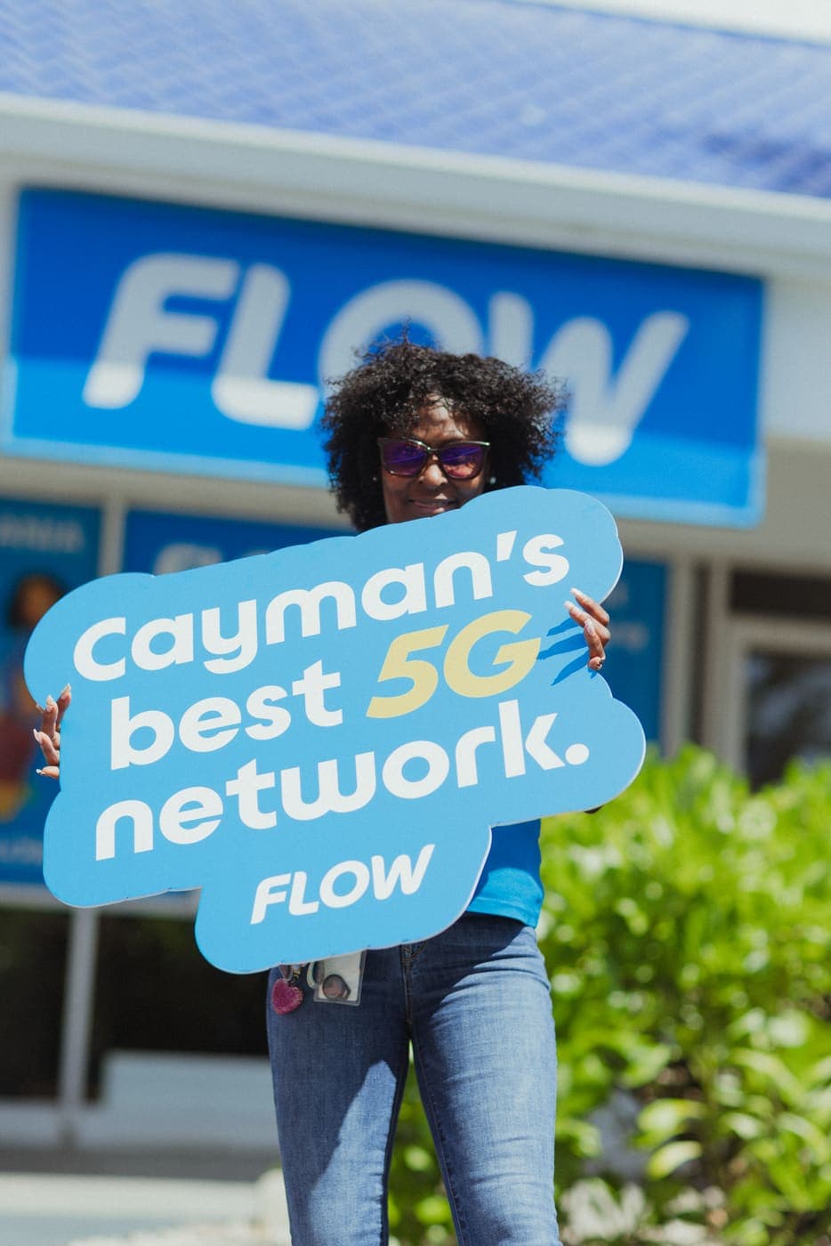A Flow team member outside the store holding a sign that reads Cayman’s best 5G network