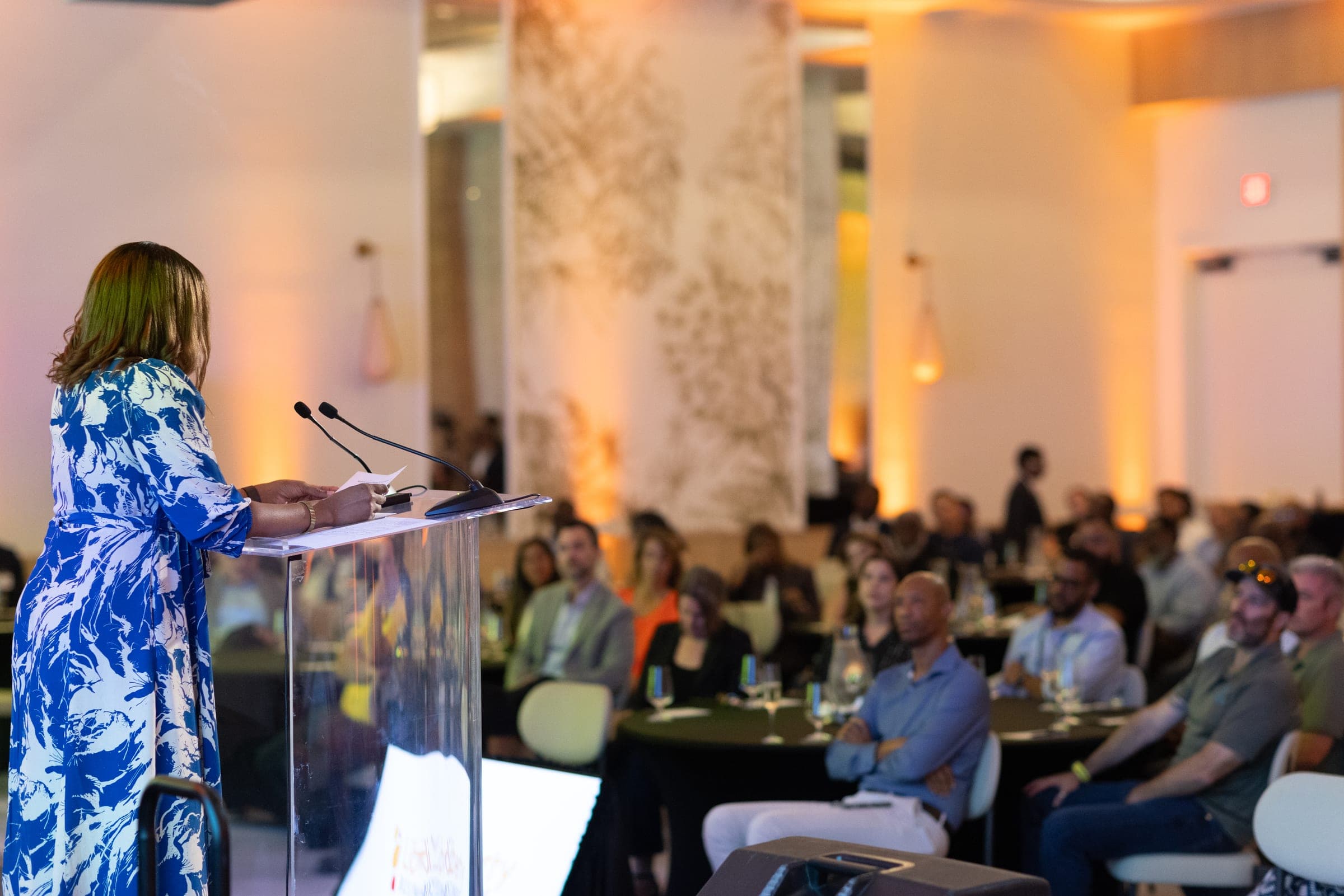 The host speaks from a clear podium to a ballroom full of seated guests at the Liberty Business launch