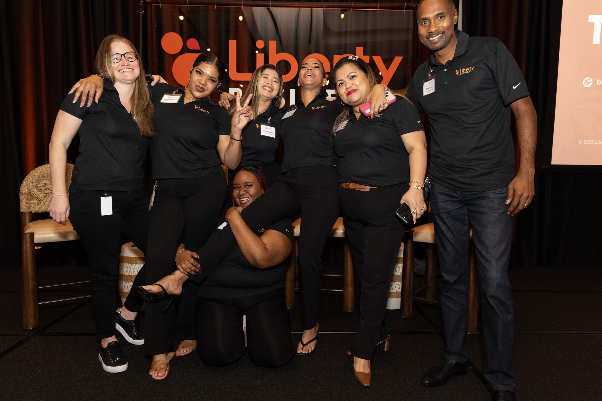 Liberty Business staff in branded polos pose together on stage in front of the company logo