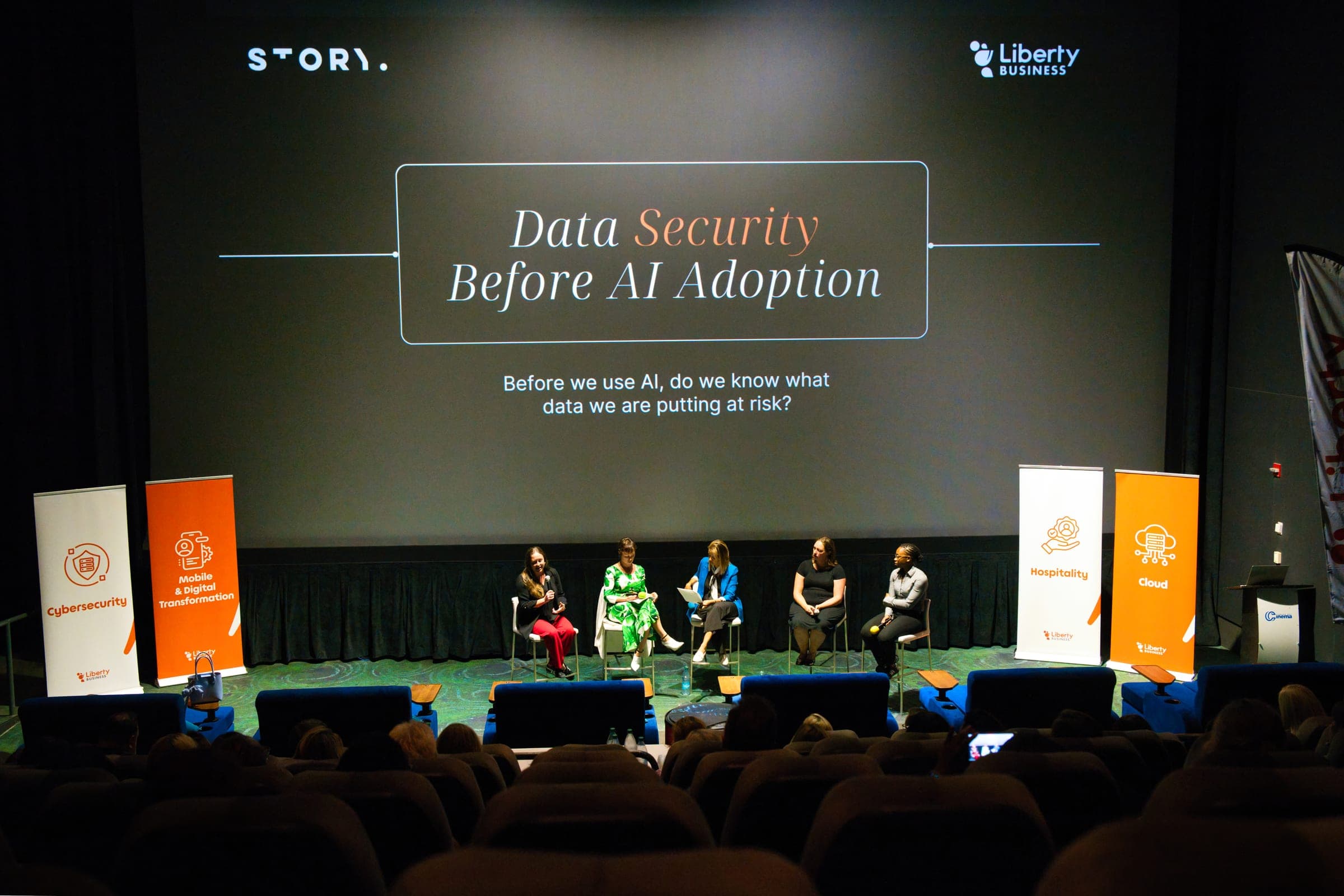 Five panellists on a cinema stage under a Story and Liberty Business title slide, flanked by branded banners