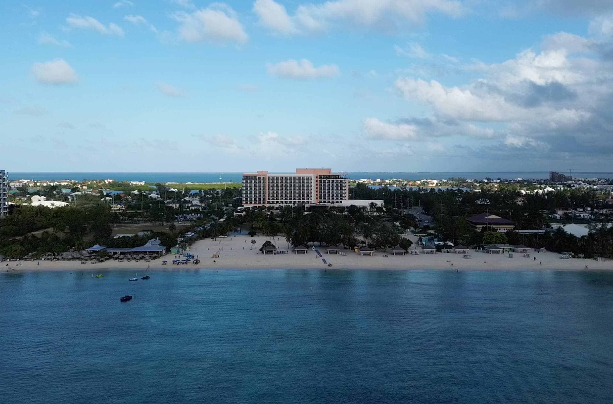 Drone view over turquoise water towards Seven Mile Beach and a beachfront hotel in Grand Cayman
