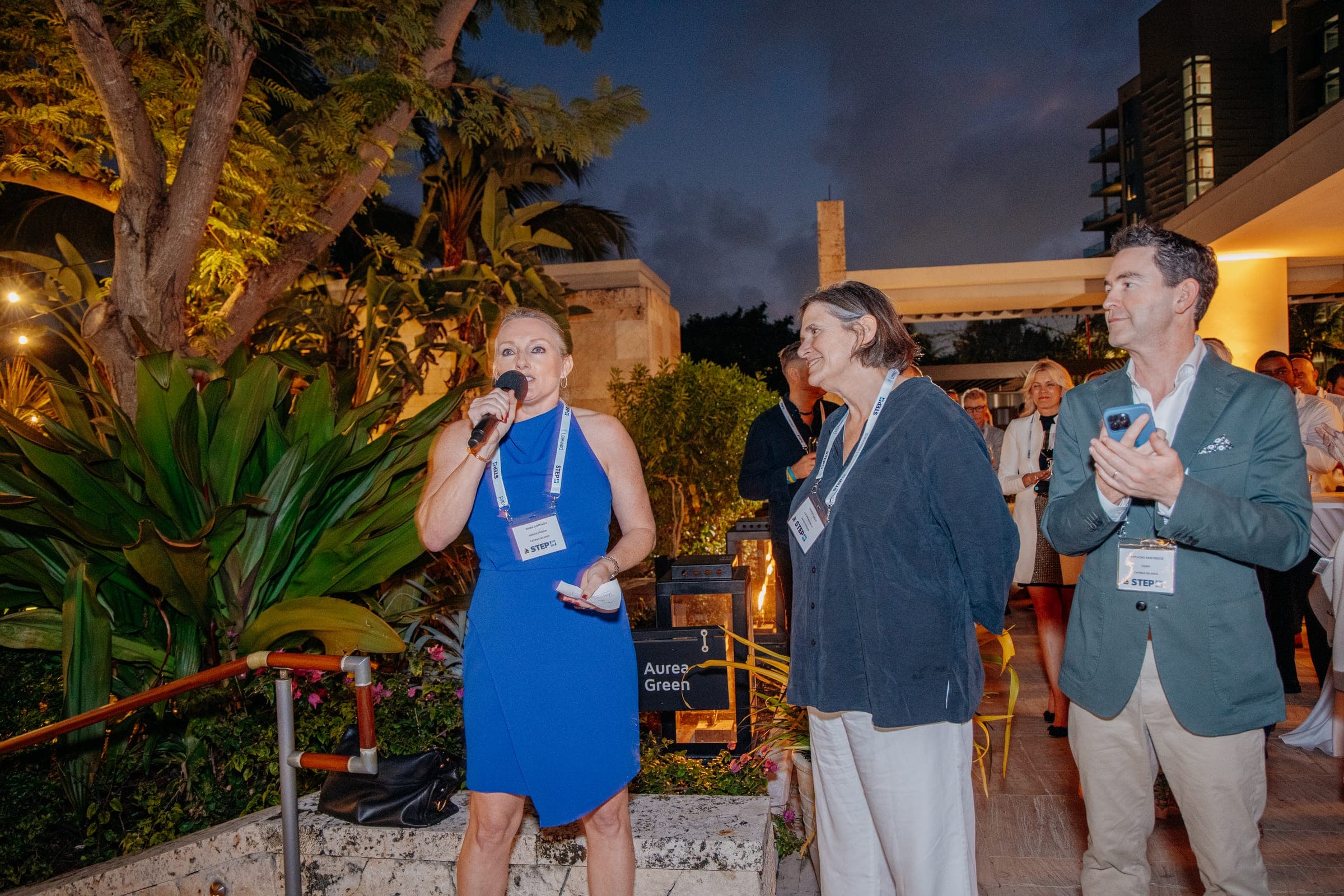 A host speaks into a microphone beside two colleagues at the evening reception